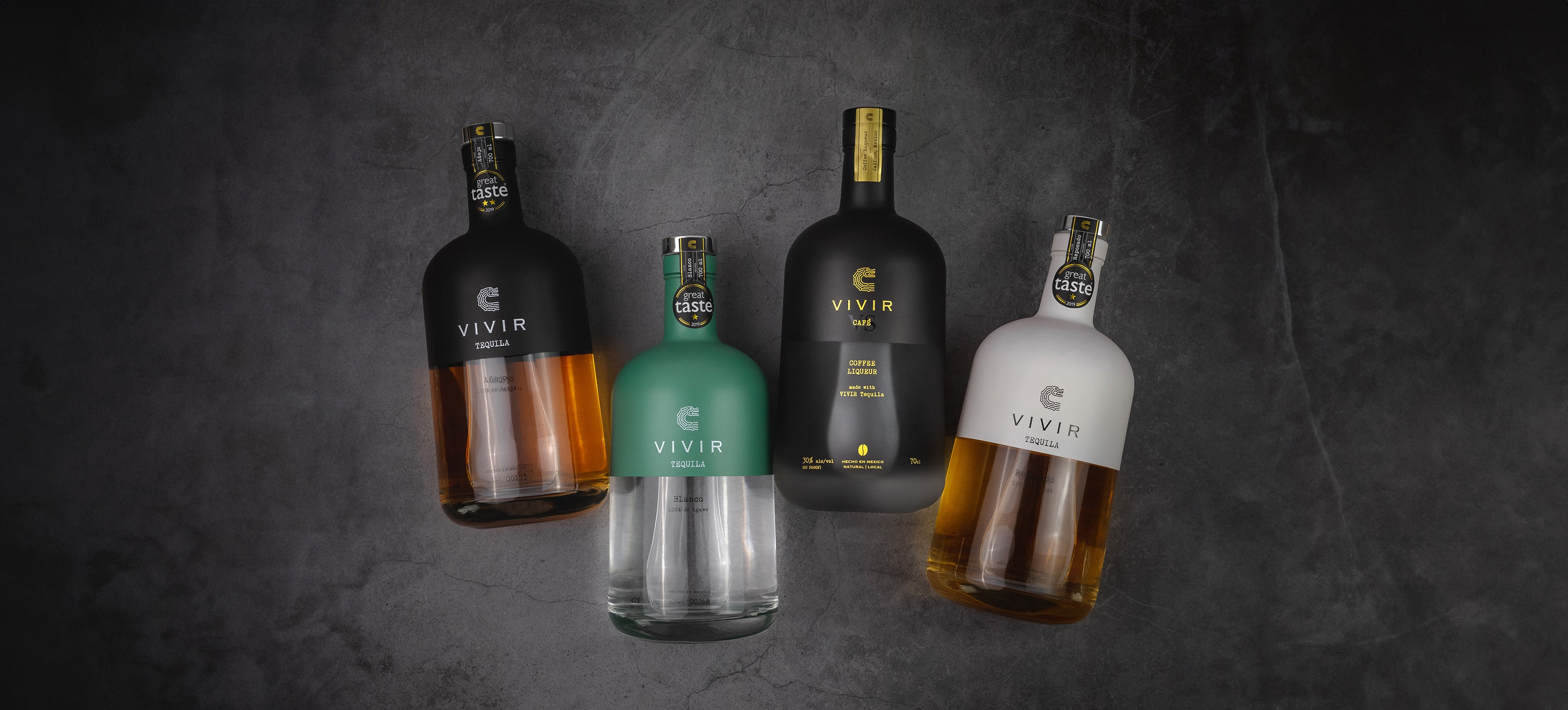 The four bottles of VIVIR Tequila are shown on a dark concrete background.