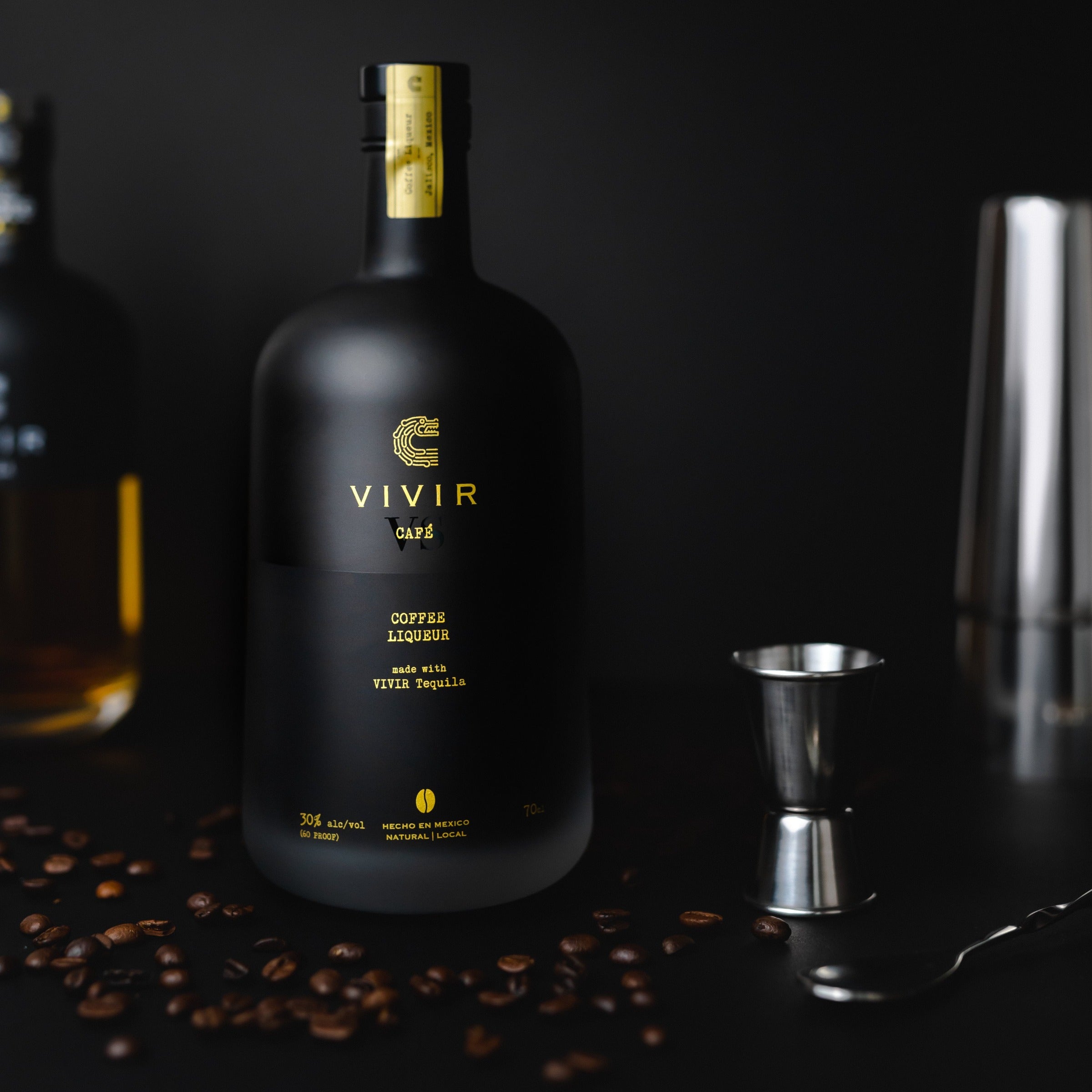 A bottle of VIVIR Café VS surrounded by coffee beans and cocktail making equipment.