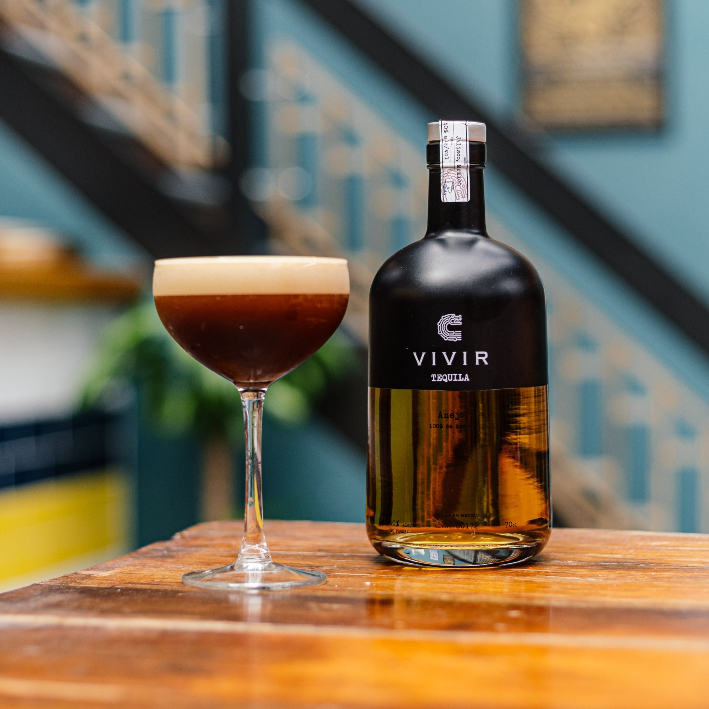 A bottle of VIVIR Tequila Anejo is positioned next to an Espresso Martini cocktail.
